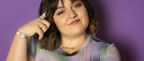 Teresa Reichl steht vor einer lilafarbenen Wand, sie lächelt in die Kamera und stützt ihren Kopf auf ihre Finger.