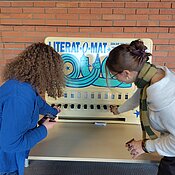 Zwei Menschen stehen vor Zigarettenautomat, der zu Literaturautomat umgestaltet ist. Sie probieren ihn aus und drücken einen Hebel.