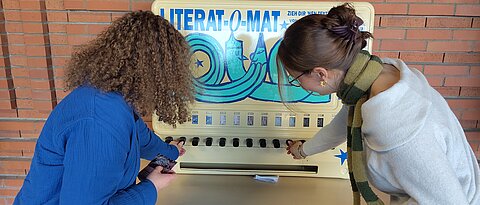 Zwei Studierende stehen vor dem Literat-O-Maten und ziehen eine Schachtel.